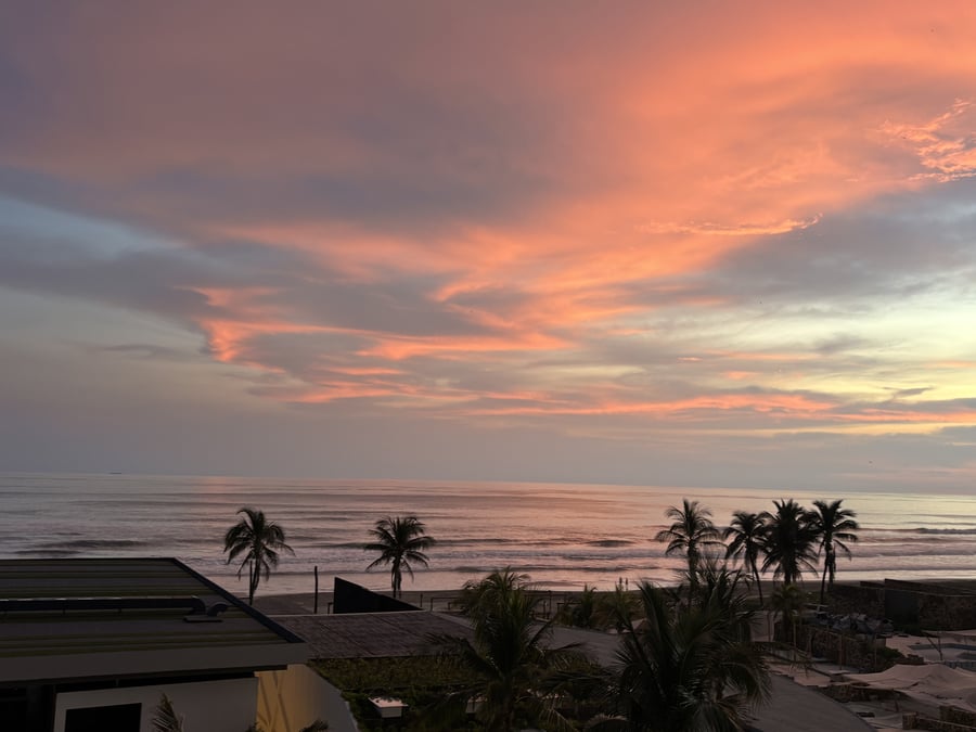 Atardecer tropical con palmeras y vista al mar desde un resort.